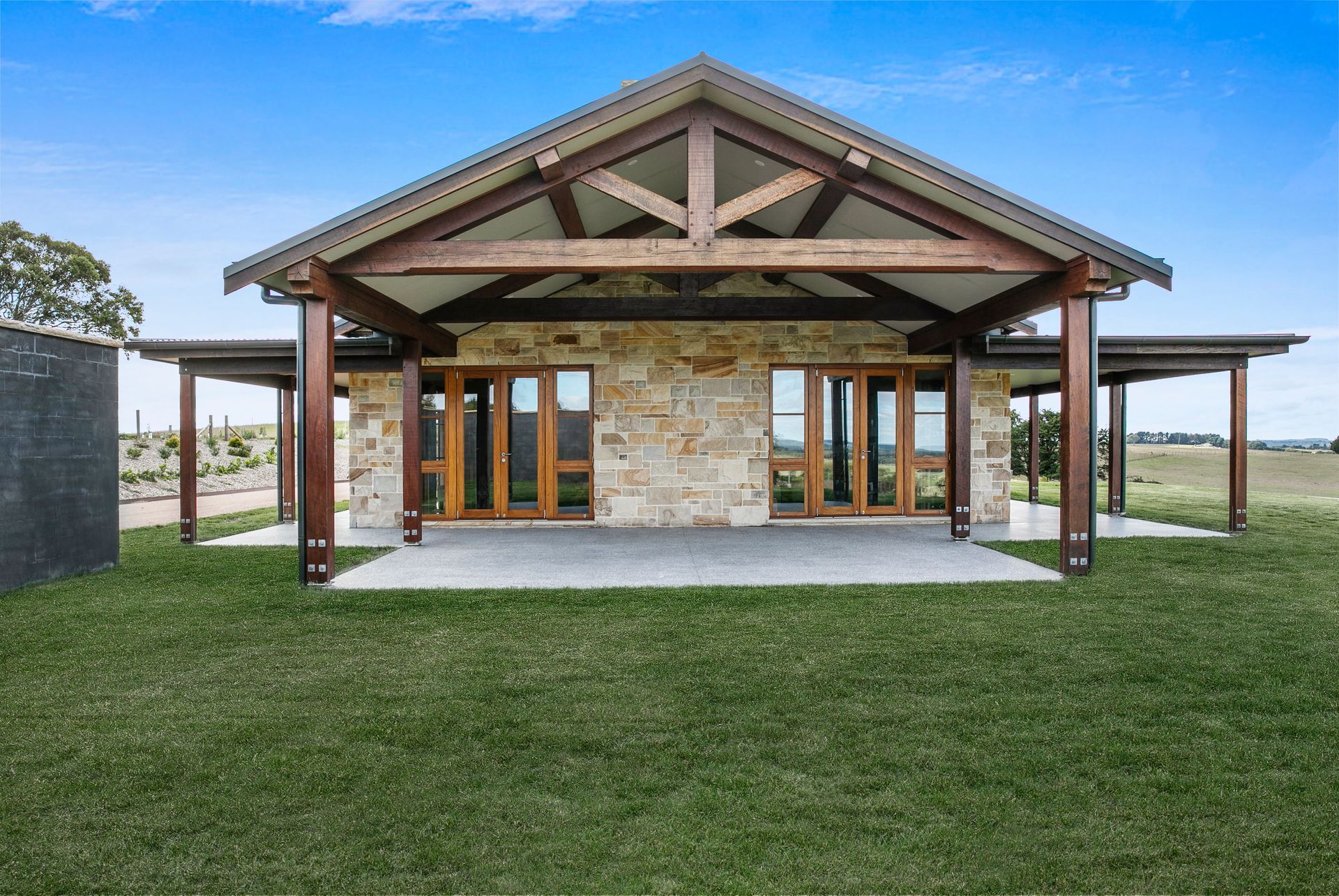 Modern stone-and-wood house with a covered front porch and green lawn under a blue sky