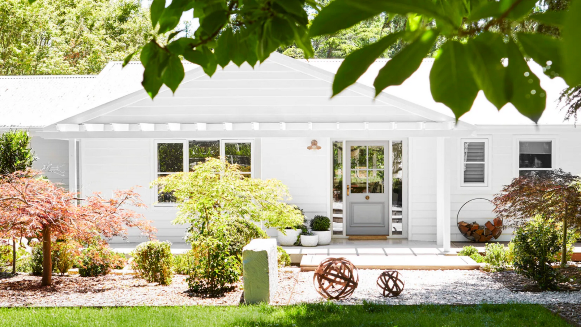 White suburban house with front garden, green lawn, and leafy tree branches overhead