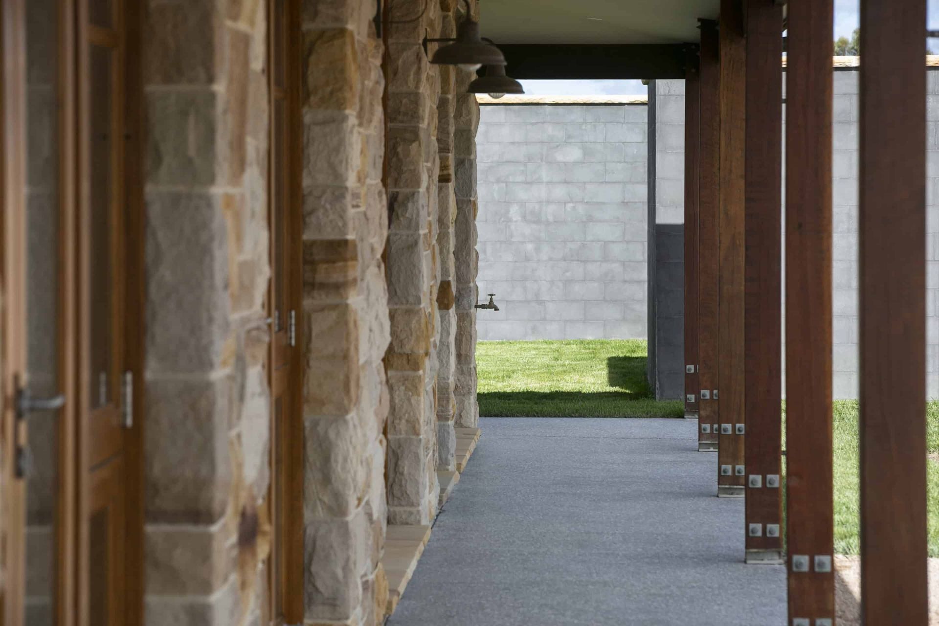 Stone-and-wood covered walkway with columns and a view of grass and a wall at the end