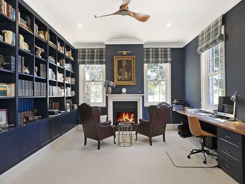 Blue home office with built-in bookshelves, fireplace, and two chairs by a window and desk