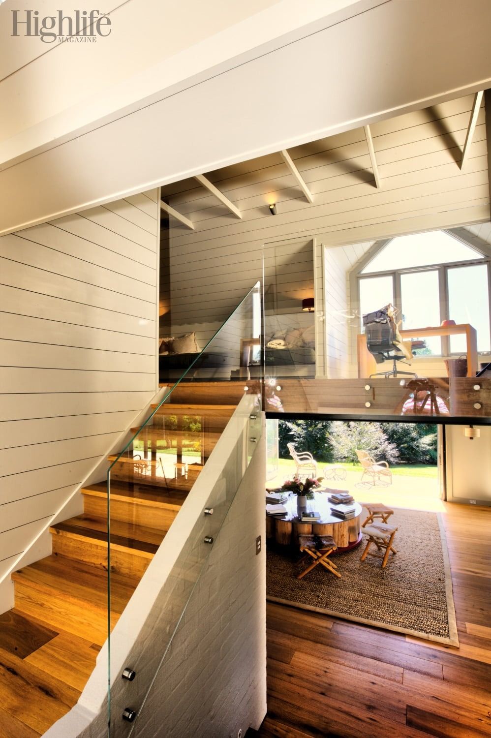 Modern open staircase overlooking a bright living room with wood floors, white walls, and large windows