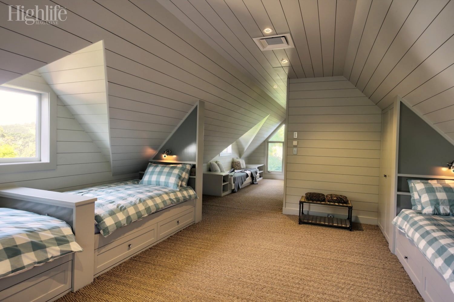 Cozy attic bedroom with two twin beds, sloped white ceiling, beige carpet, and a small chair by the window