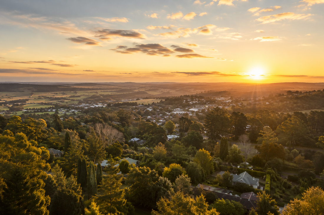 Sunset over a valley and town, with golden light illuminating trees and distant hills