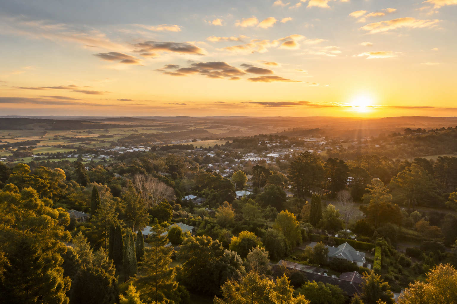 Sunset over a valley with trees, houses, and distant hills under a golden sky
