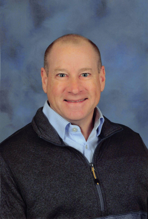 David Rust - Portrait of a smiling person in a dark jacket against a blue studio backdrop