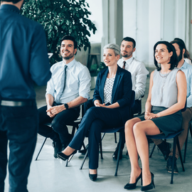 People seated in a bright office listening to a speaker during a presentation