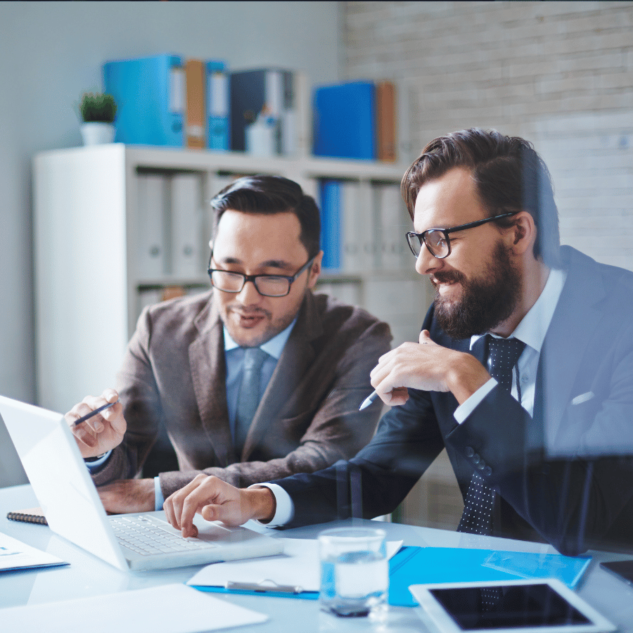 Two professionals reviewing documents at a desk with a laptop in a bright office