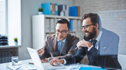 Two people in a meeting with charts, speech bubbles, and a document, discussing ideas in a workspace.