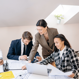 Two professionals reviewing documents at a desk with a laptop in a bright office