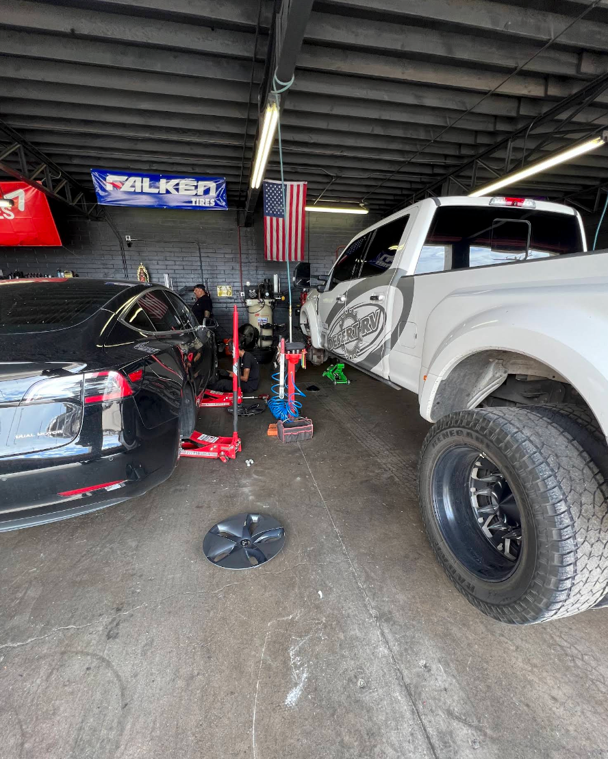 Black car and lifted white pickup in an auto shop with tools and an American flag. | TireUp Tires| Wheel Alignment, Brakes & Service