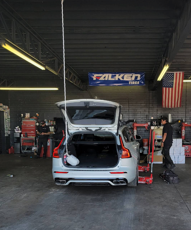 Silver SUV with open hatch in an auto garage, with tools, mechanics, Falken banner, and an American flag. | TireUp Tires| Wheel Alignment, Brakes & Service