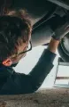 Mechanic working under a car, wearing gloves and glasses.