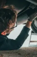 Mechanic working under a car, wearing gloves and glasses.