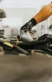 Hand pouring oil from a container into a car engine, in a mechanic shop setting.