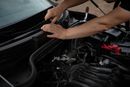 Hands working on a car engine, possibly replacing weather stripping.