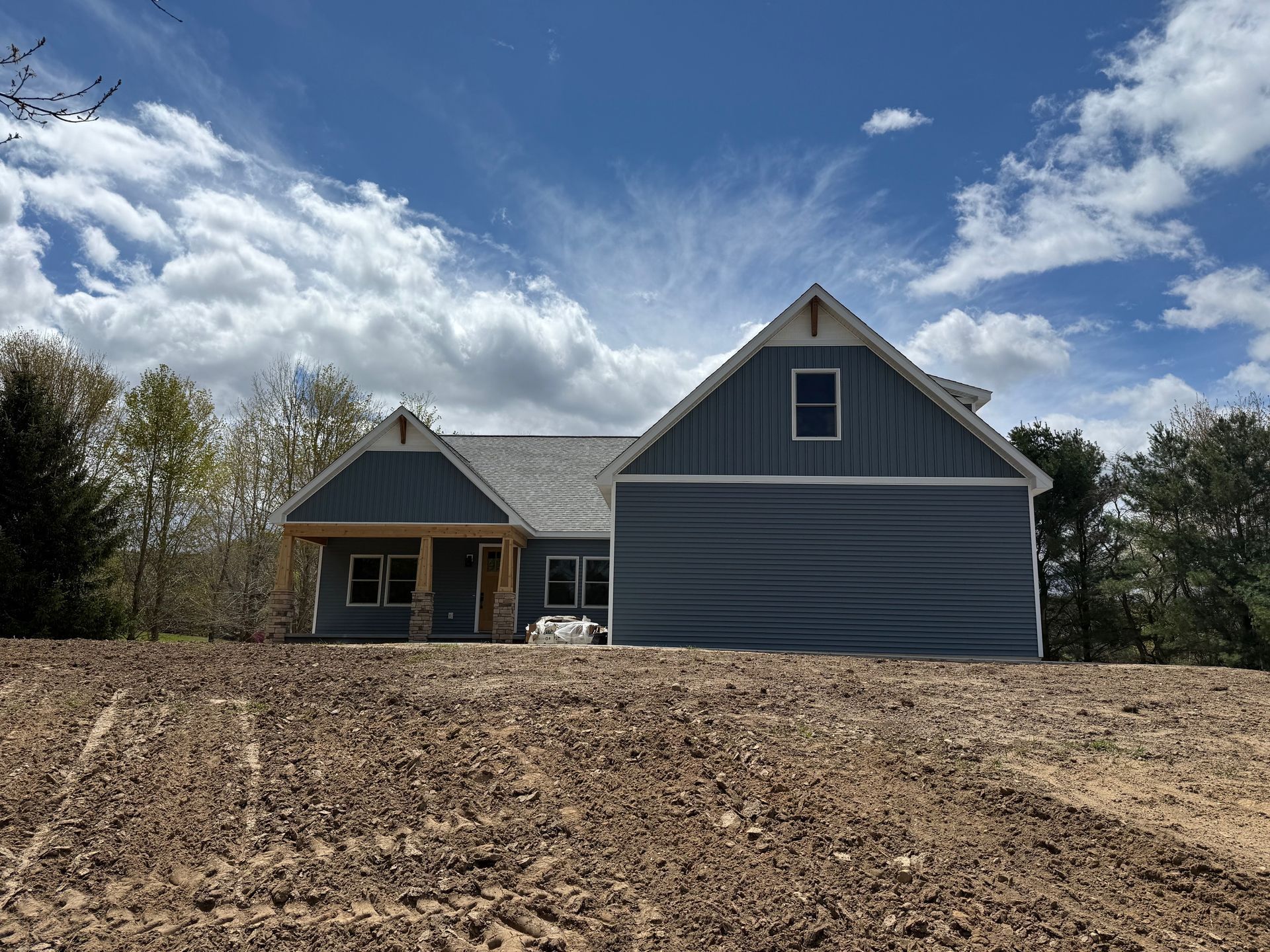 New gray house with gabled roof and front porch under a partly cloudy sky