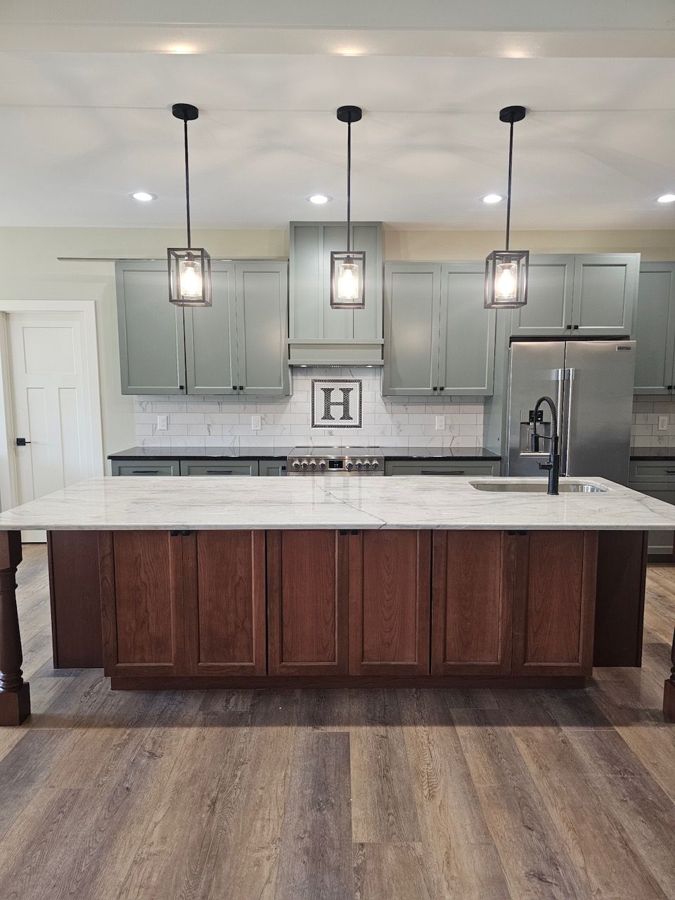 Modern kitchen with gray cabinets, white island, pendant lights, and wood-look flooring