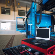Red equipment cart with laptop beside a blue industrial vehicle inside a workshop