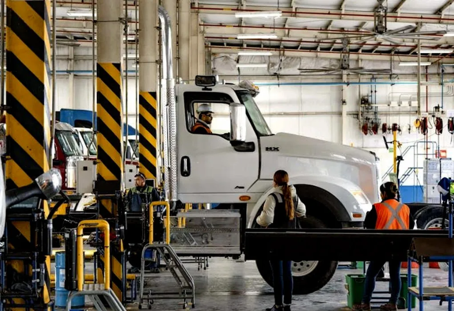 Truck assembly line in a factory, with workers beside a white semi-truck chassis