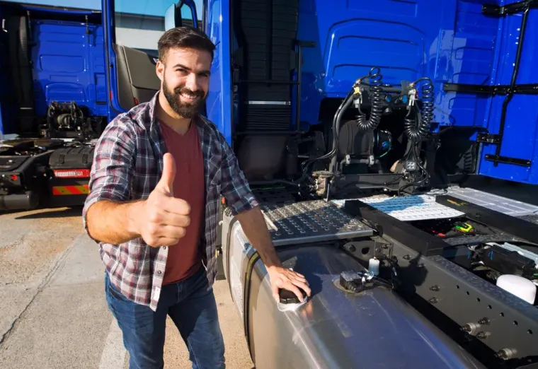 Smiling man giving a thumbs-up beside a vehicle chassis in a blue-lit workshop