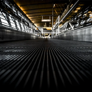 Low-angle view down an industrial walkway with metal grating and bright overhead lights