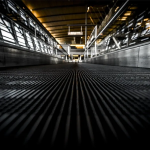 Low-angle view down an industrial walkway with metal grating and bright overhead lights