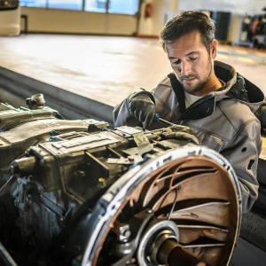 Mechanic inspecting a large engine or transmission in a workshop, wearing gloves and a gray jacket