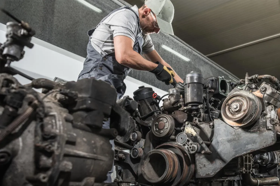 Mechanic working on a large engine in a workshop, surrounded by disassembled metal parts