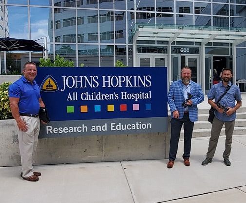 Three men standing in front of a johns hopkins all children 's hospital sign