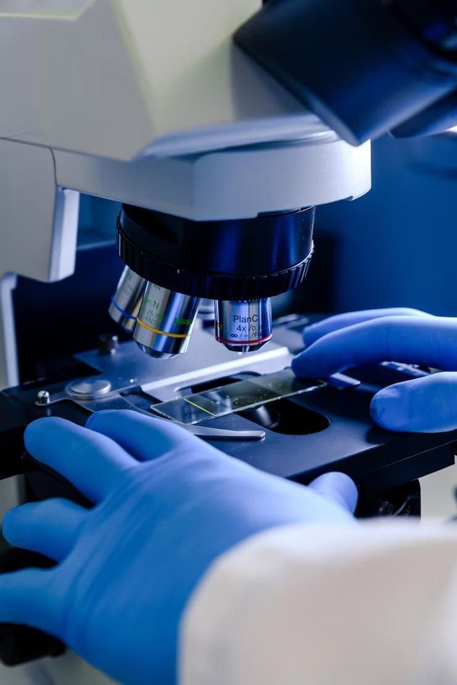A person wearing blue gloves is looking through a microscope.