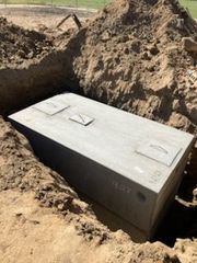 Concrete rectangular tank installed in a dirt trench, three access hatches visible.