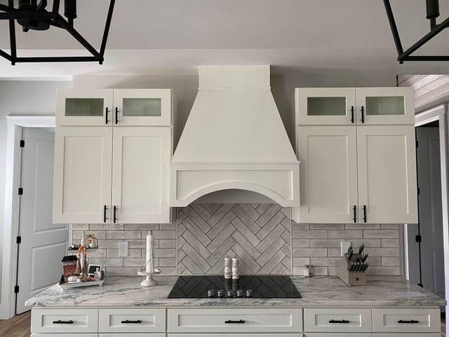 Bright white kitchen with cabinets, marble backsplash, island sink, and black pendant lights.