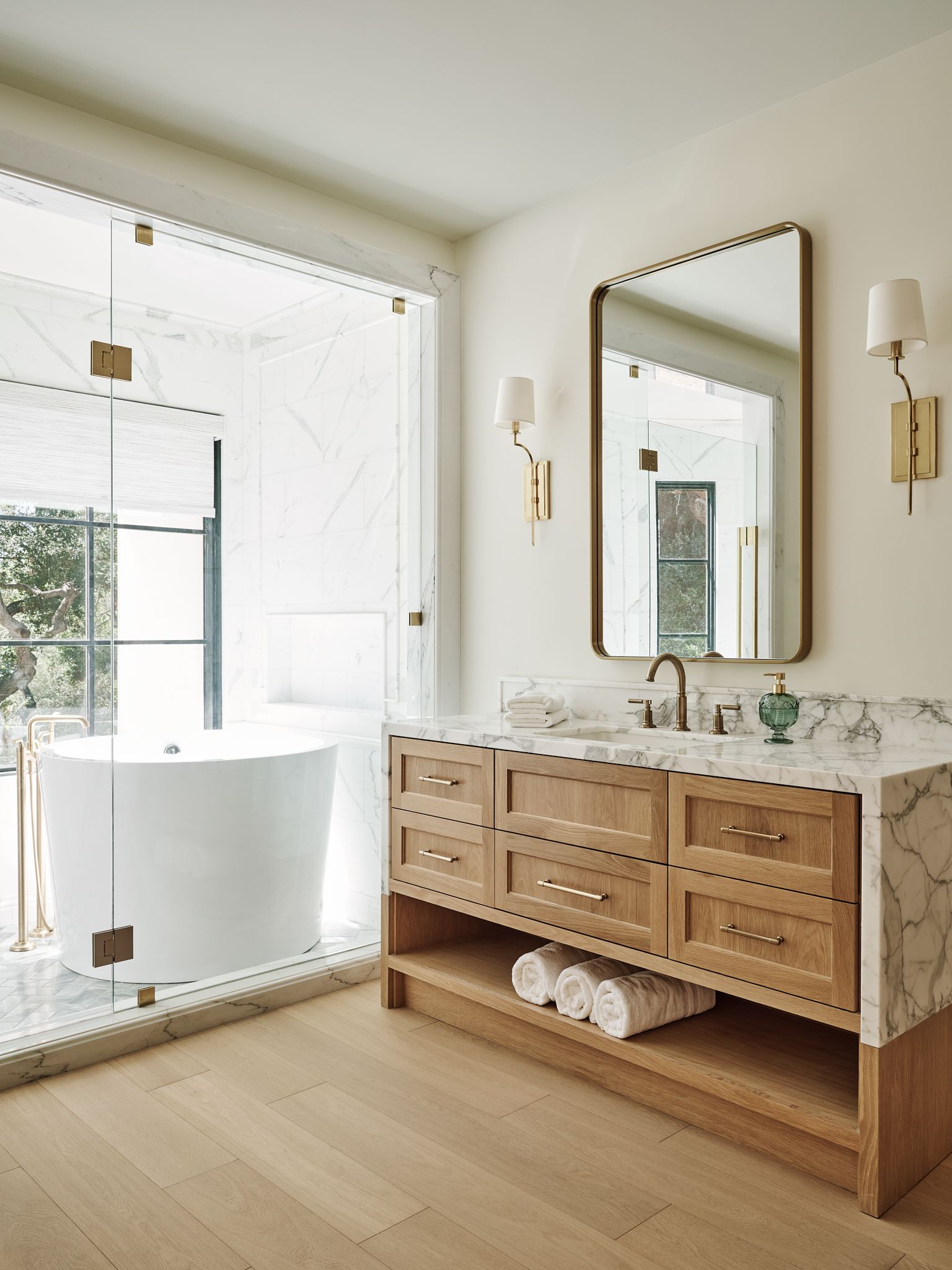 Bathroom with geometric tile floor, white vanity, gold mirror, black tiled wall, glass shower, and freestanding tub.