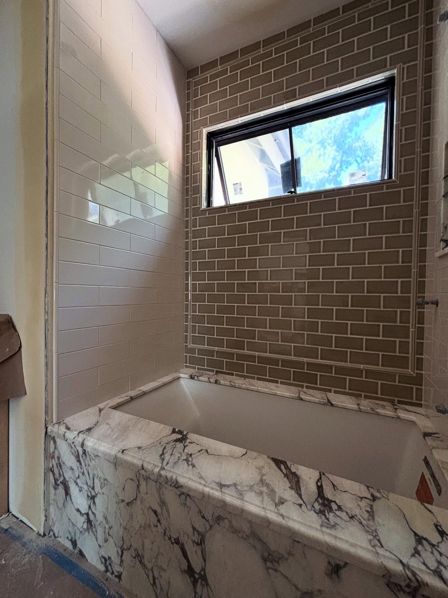Bathroom with bathtub and tile in various colors, window above, marble-like trim.