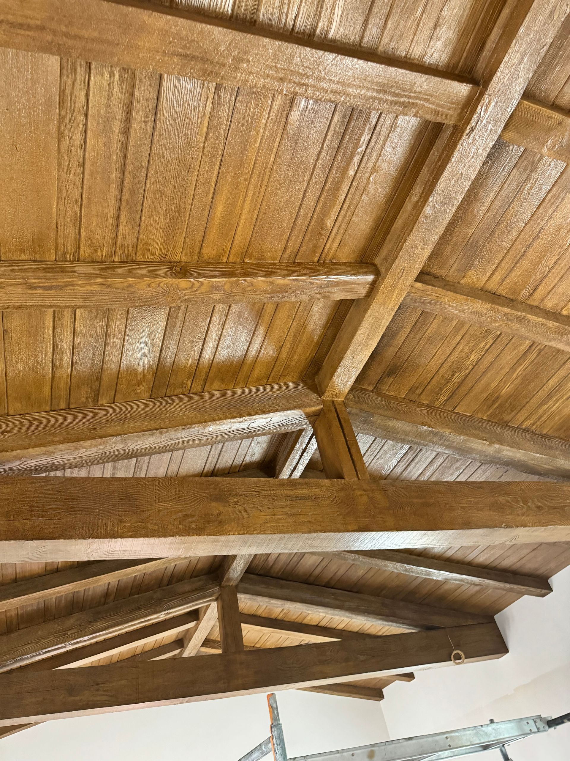 A low-angle view of a wooden vaulted ceiling with exposed beams and wood-paneled rafters in a warm, honey-toned finish.