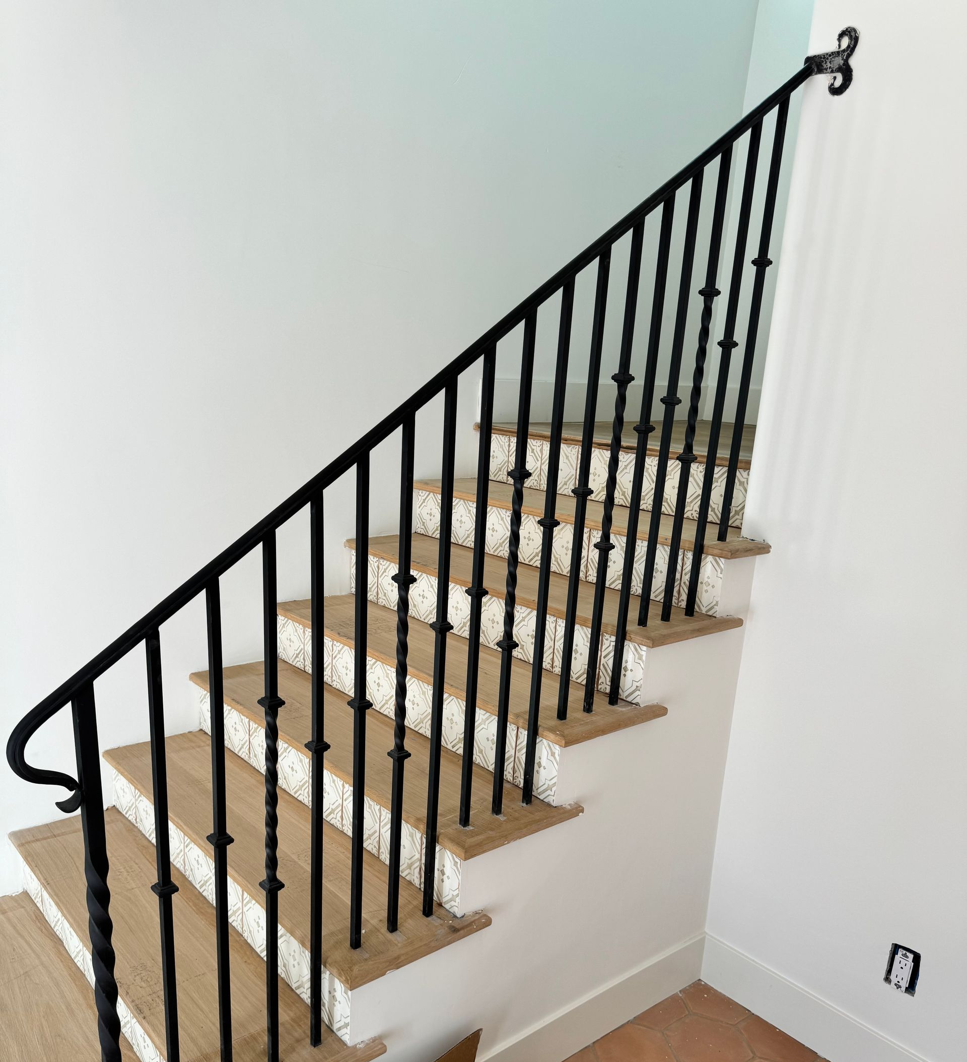 A staircase with beige carpeted steps and a decorative black wrought iron railing against a white wall.