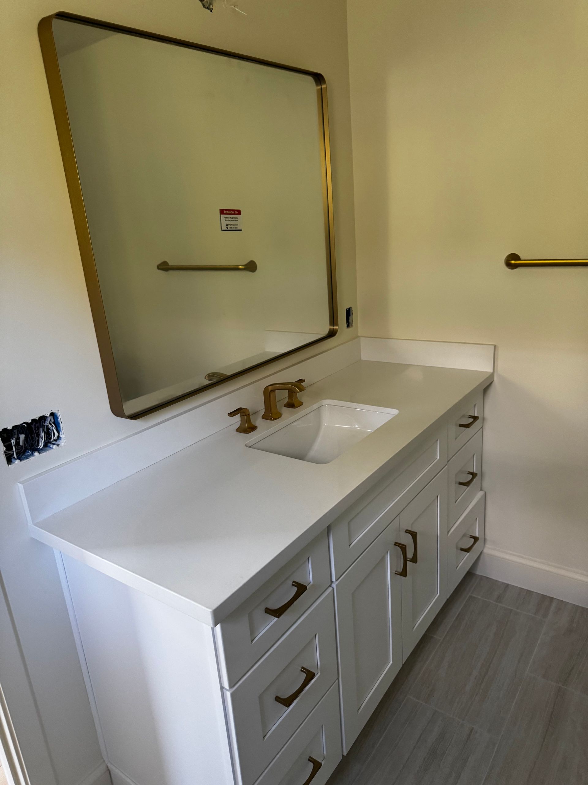 White bathroom vanity with gold hardware, a rectangular mirror, and a single sink against a beige wall.