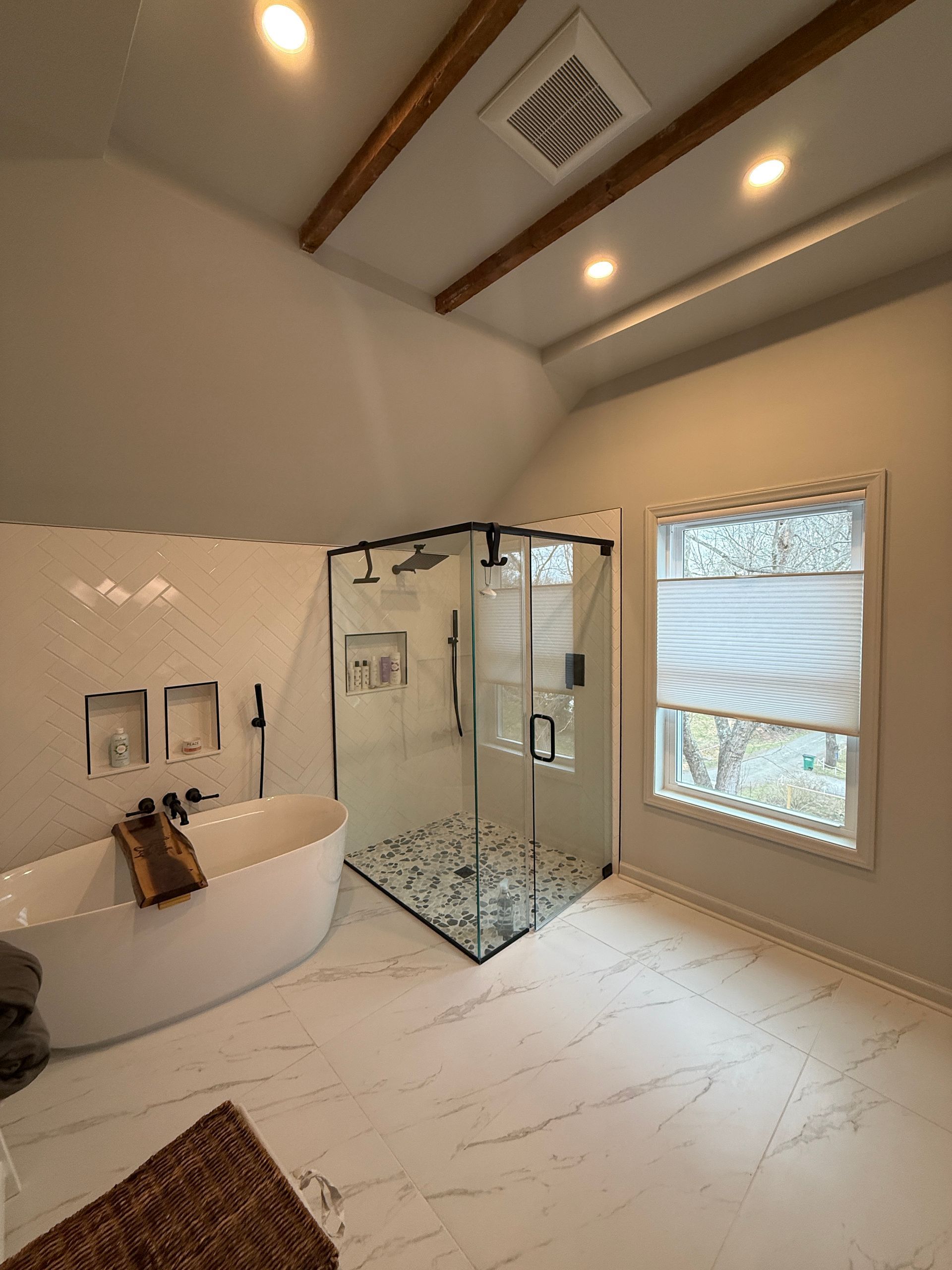 Modern bathroom with freestanding tub, glass shower, marble tile, and window blinds
