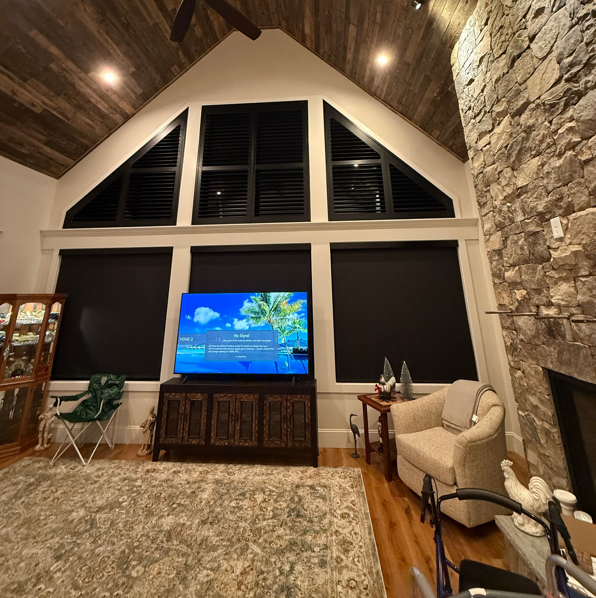 Living room with vaulted wood ceiling, stone wall, large windows, TV, and cozy seating