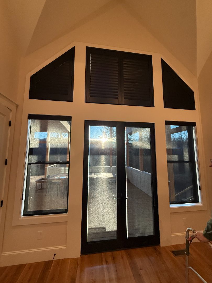 Interior view of a room with tall windows and black framed doors. Sunlight streams through.