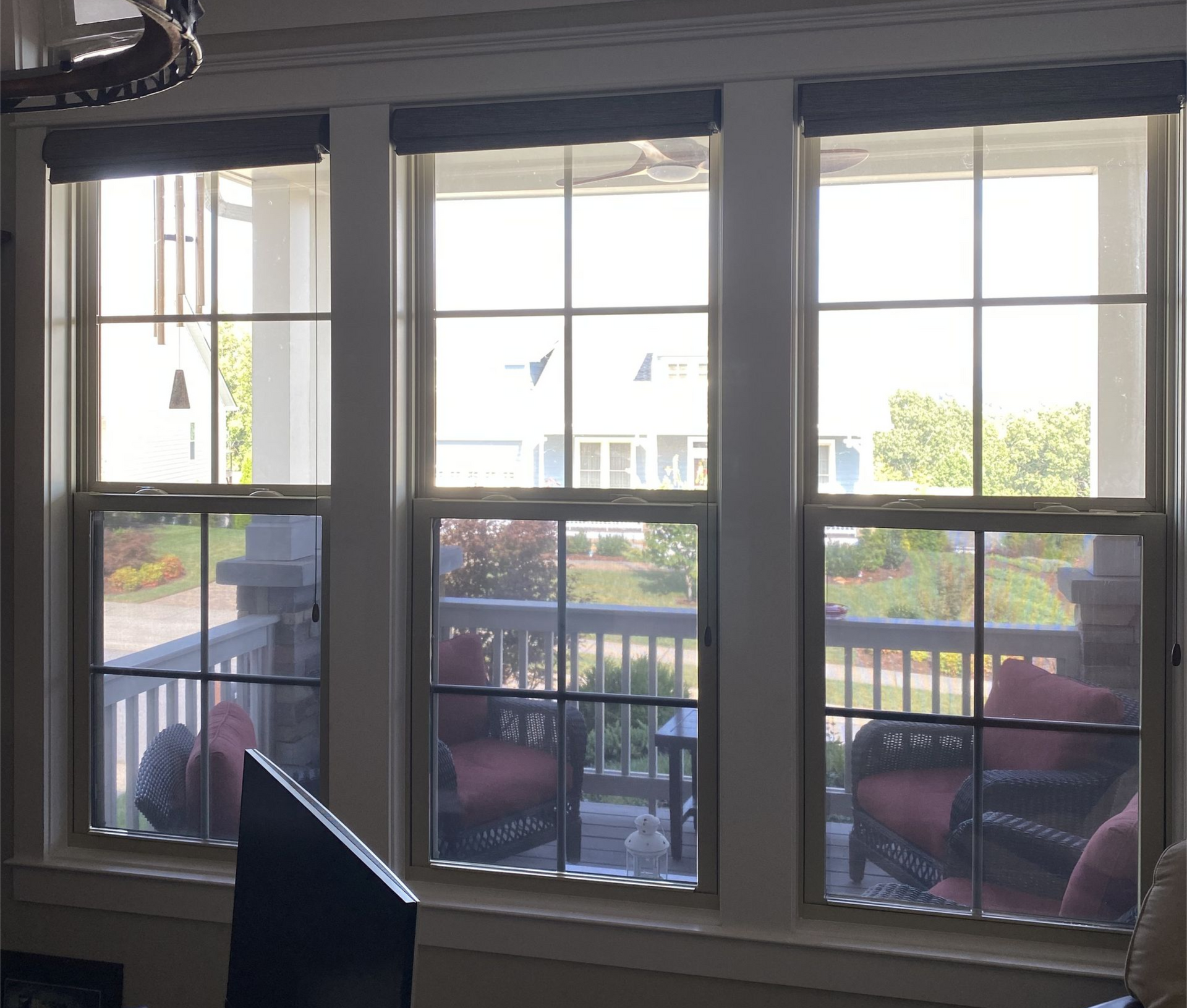 Sunlit living room windows overlooking a balcony with red chairs and a railing