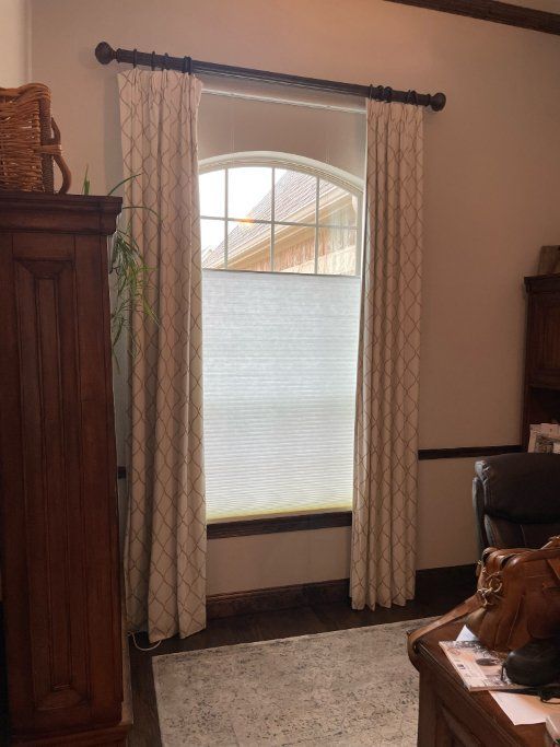 Living room with a tall arched window, beige curtains, and dark wood furniture