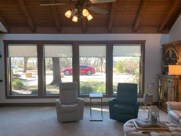 Cozy living room with two chairs, large windows, wood ceiling, and a red car visible outside.