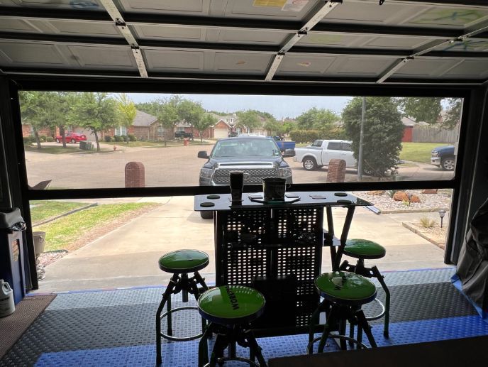 Garage view of a patio table and green stools facing an open driveway and street
