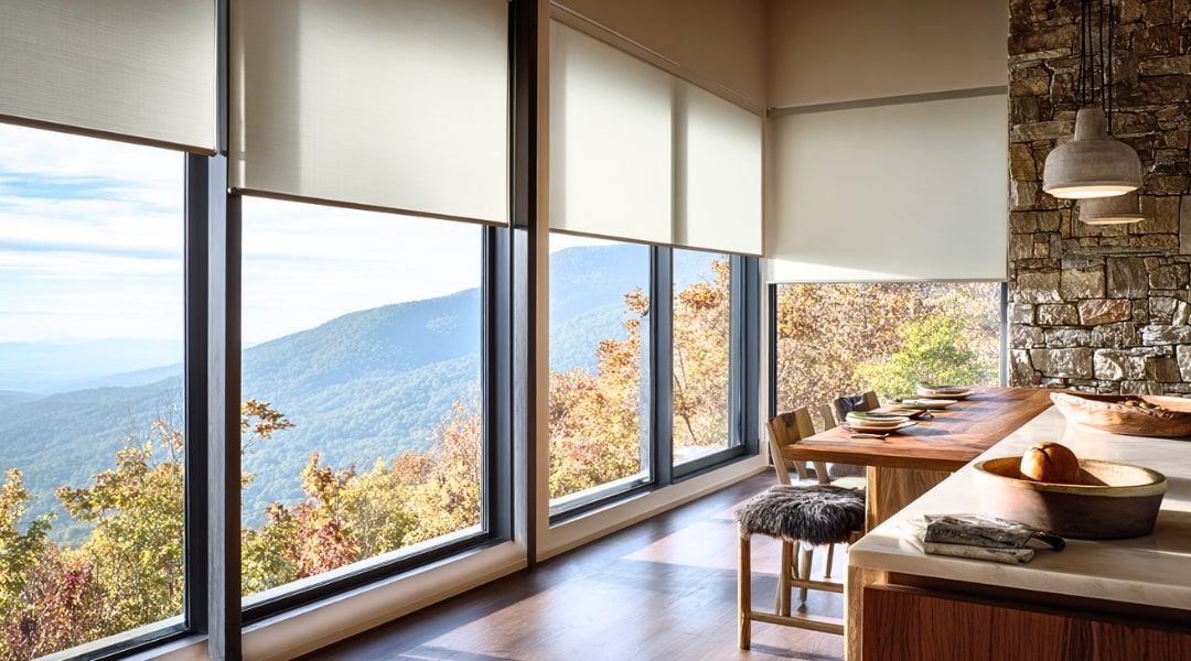 Modern room with large windows overlooking a lake and mountains, wooden table, and bench seating
