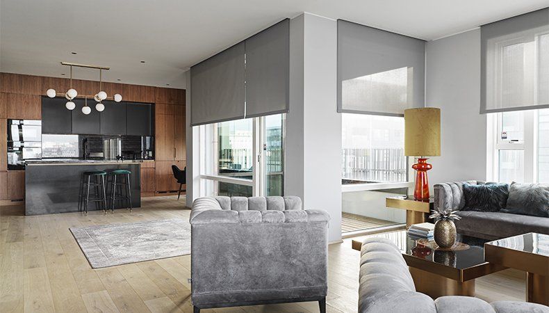 Modern open-concept living room and kitchen with gray furnishings, wood accents, and large windows