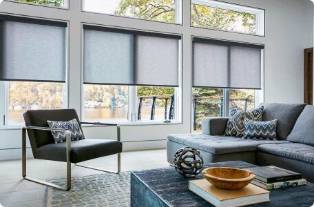 Modern living room with gray sofa, black chair, and large windows with blinds