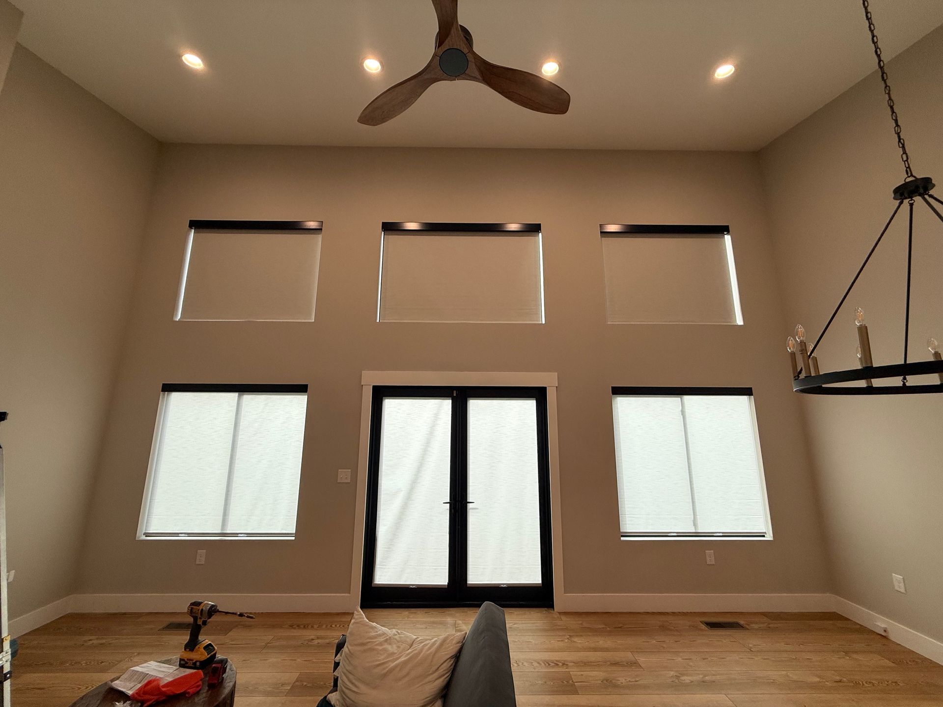 Empty beige living room with tall windows, double glass doors, wood floor, and ceiling fans