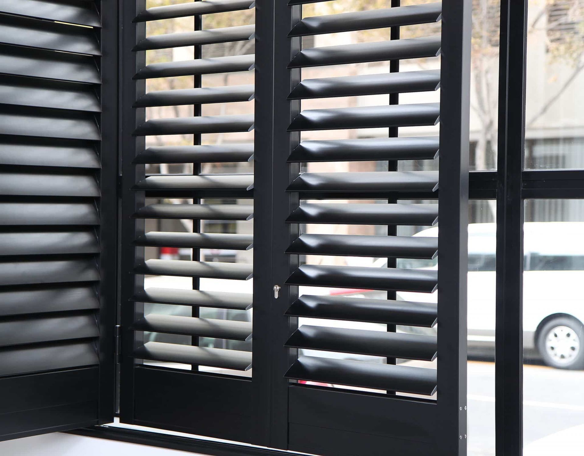 Black slatted window shutters overlooking a street with parked cars outside.