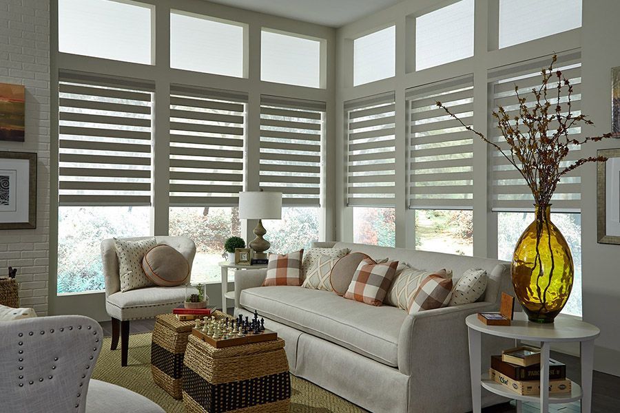 Bright living room with white sofa, armchair, striped blinds, and a large amber vase on a side table